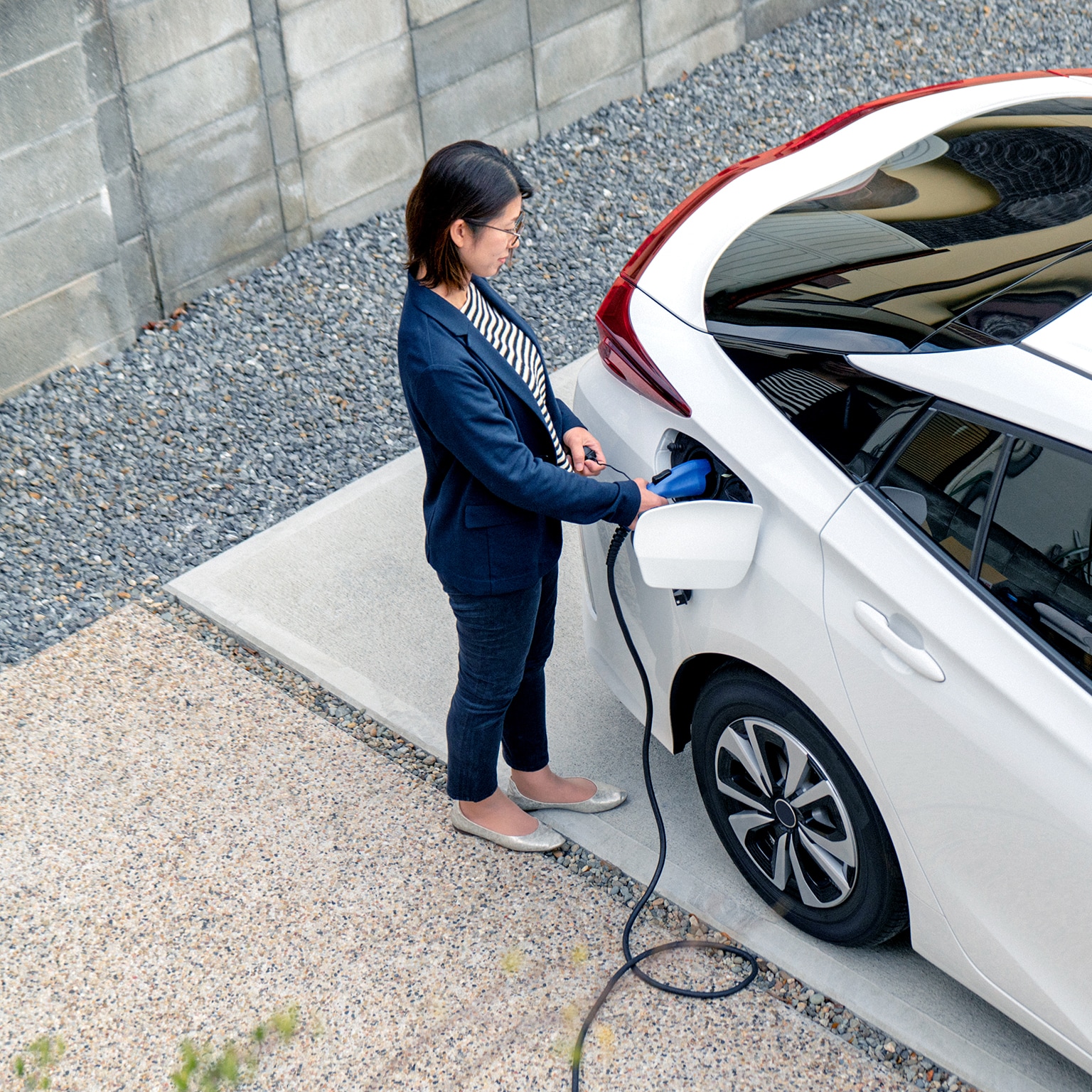 Mid adult woman charging her electric car at home - stock photo