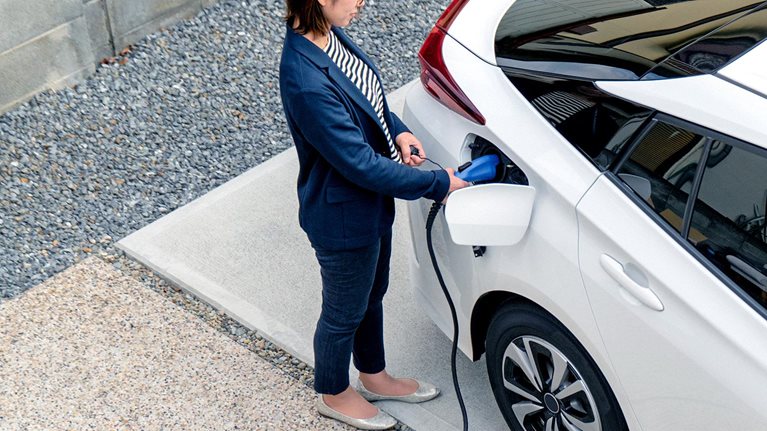Mid adult woman charging her electric car at home - stock photo