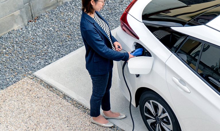 Mid adult woman charging her electric car at home - stock photo