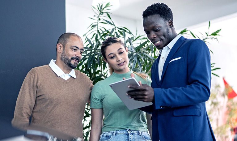 Car salesman using digital tablet talking about new car to customers in a store