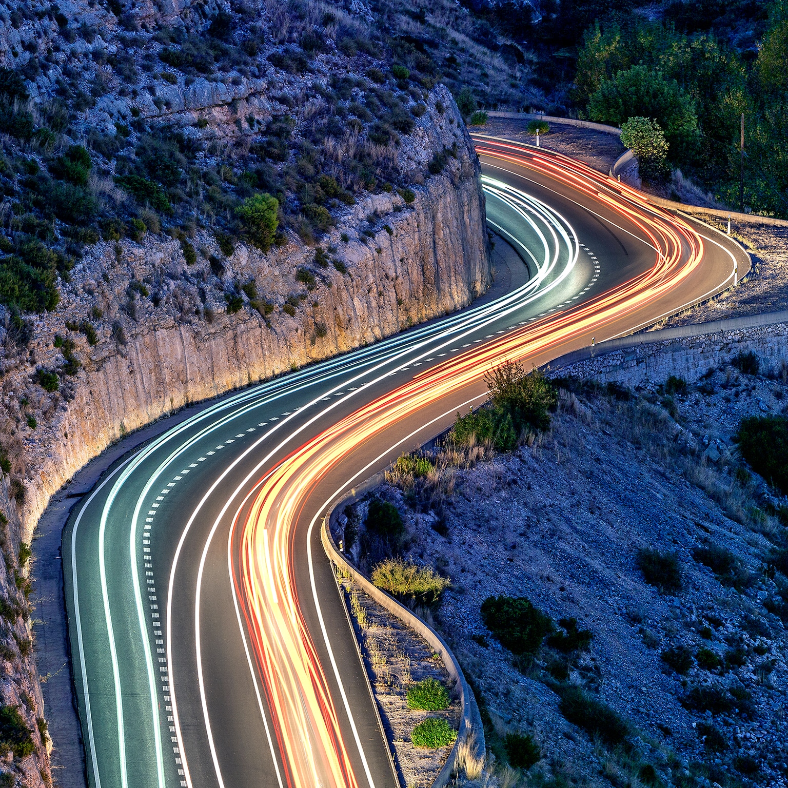 A high angle of a light trails on a s-shaped mountain road at night between the towns of Bocairent and Ontinyent.