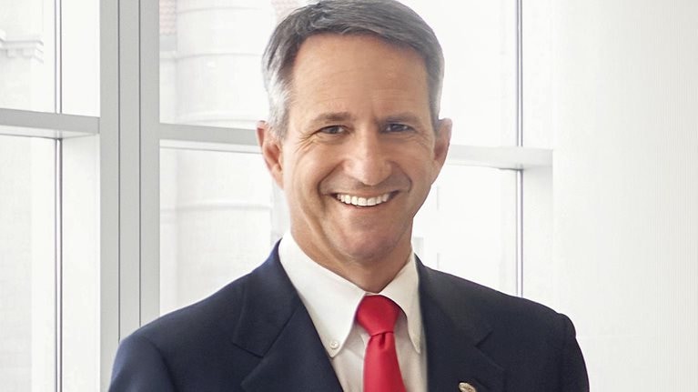 Wearing a dark blue suit, Christophe Beck, CEO of Ecolab, stands by a large window.