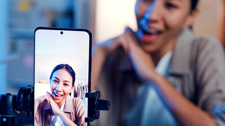 Asian woman live-streamed ecommerce sell clothes in home at night. Beautiful girl using the smartphone and tablet for recording video.