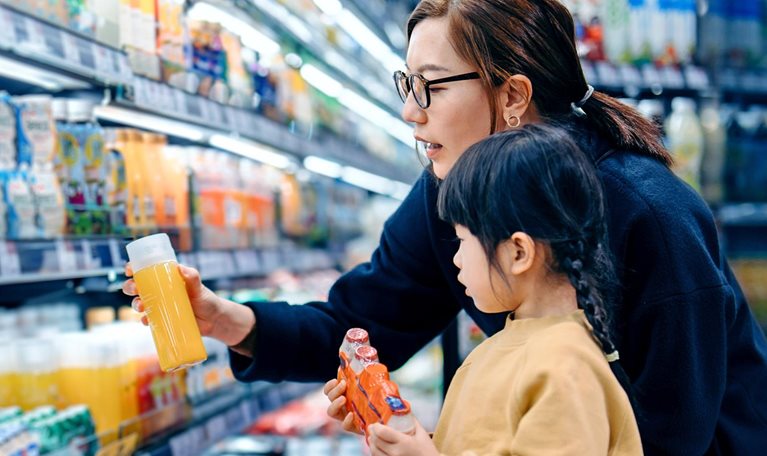 A lady and a young girl checking bottled drinks, including probiotics, from the shelves of a departmental store.