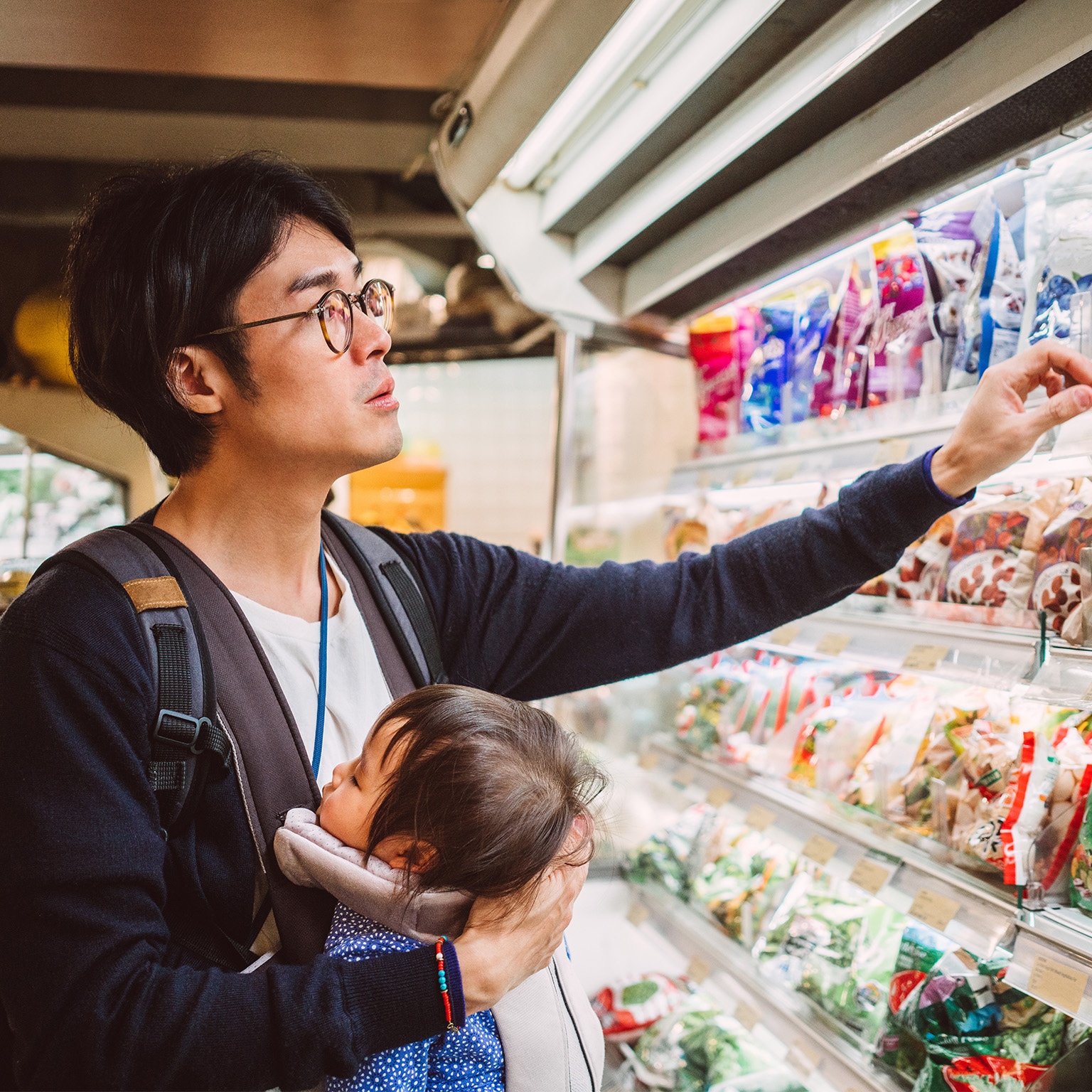 Handsome young dad carrying his baby in a baby carrier while shopping in a supermarket.