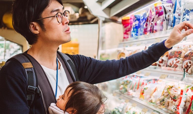 Handsome young dad carrying his baby in a baby carrier while shopping in a supermarket.