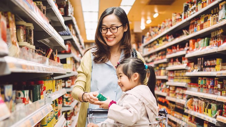 Little girl who is sitting in the trolley shopping joyfully with her mom at the supermarket.