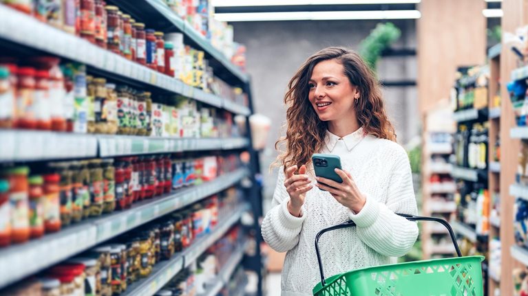 Woman using a smartphone while choosing products in the supermarket
