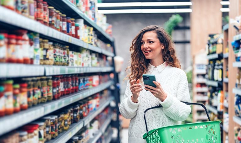 Woman using a smartphone while choosing products in the supermarket