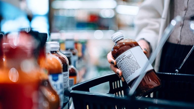 Close-up image of a woman putting a bottle into her shopping basket while shopping in a supermarket.