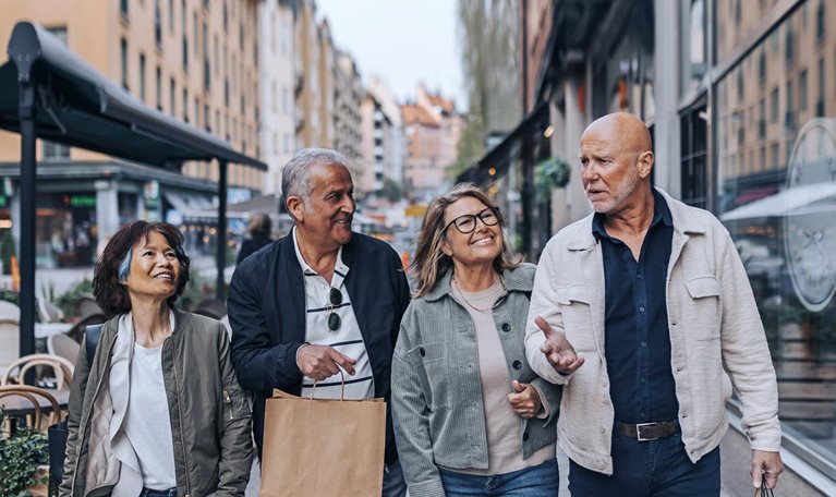 A cheerful group of senior friends strolling down a European sidewalk, engaged in conversation and carrying shopping bags.