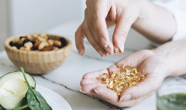 Woman Doctor Nutritionist Hands In White With Omega 3, Vitamin D Capsules With Green Vegan Food