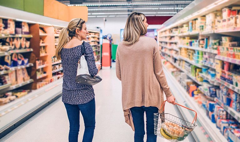 Two women walking down a grocery store aisle with a shopping basket