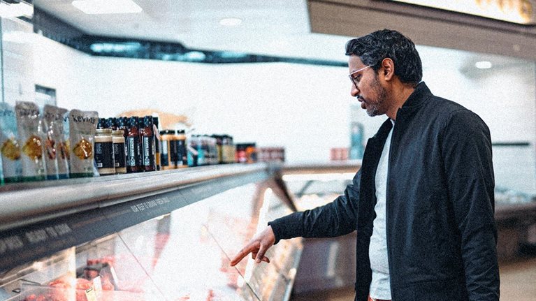 A man ordering prepared meat from the deli case of a grocery store