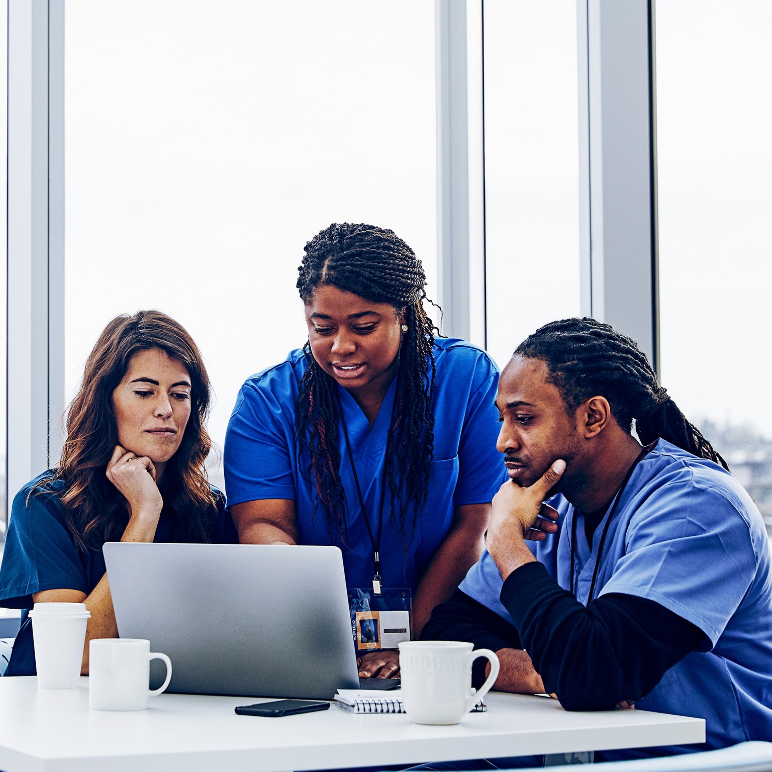 Female nurse with laptop talking to colleagues against window in hospital