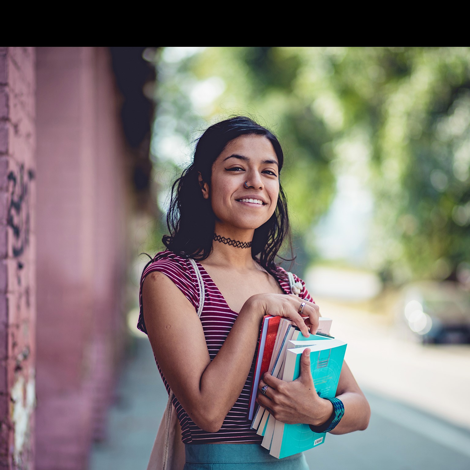 Young student woman standing on street and holding books.