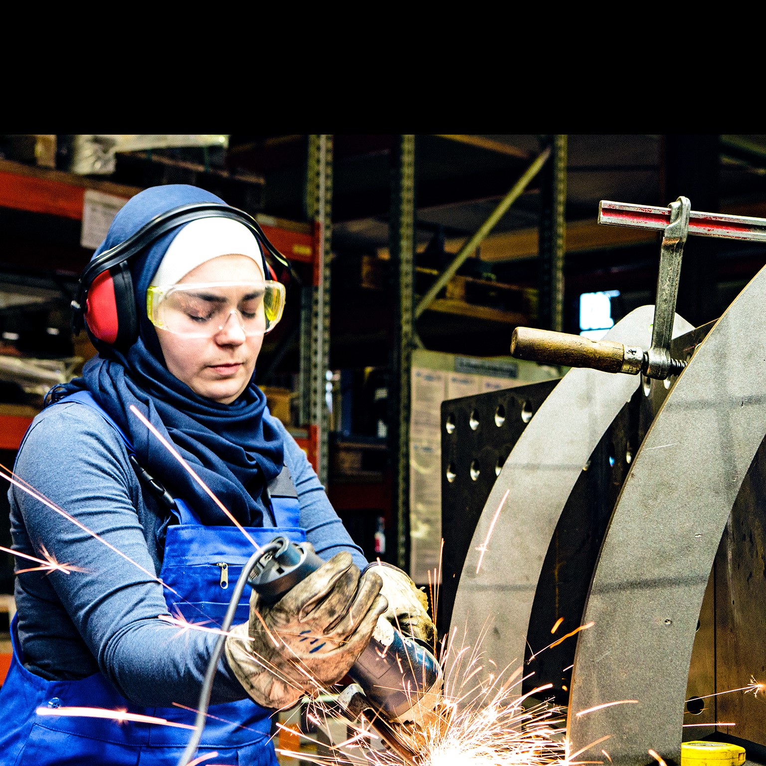 Young female trainee works with a grinder in a workshop, flying sparks