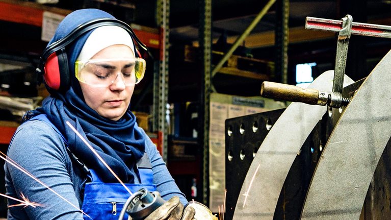 Young female trainee works with a grinder in a workshop, flying sparks