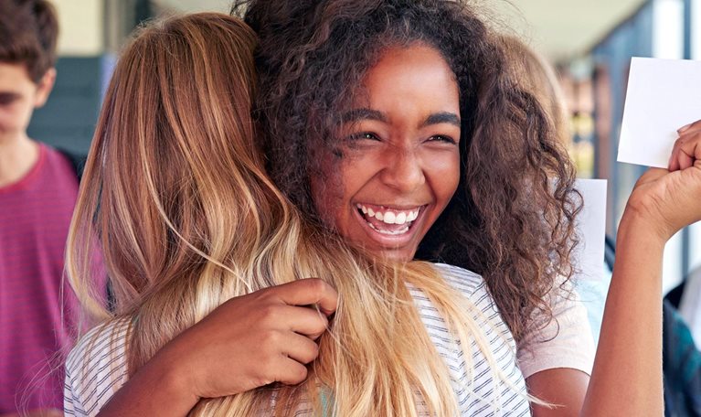 Two girls celebrating exam results in school corridor