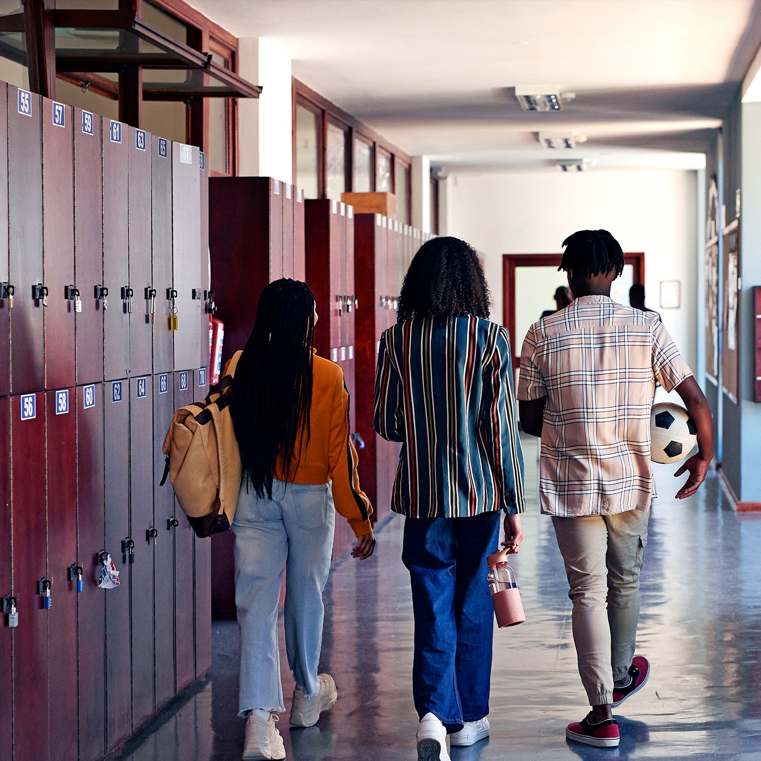 Full length rear facing view of male and female students walking together in school hallway with lockers