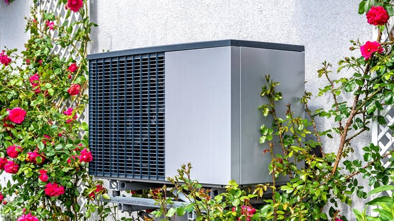 Outdoor unit of heat pump heating of residential house framed by roses