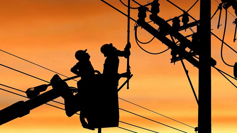 Silhouette two electricians with disconnect stick tool on crane truck are working to install electrical transmission on power pole - stock photo