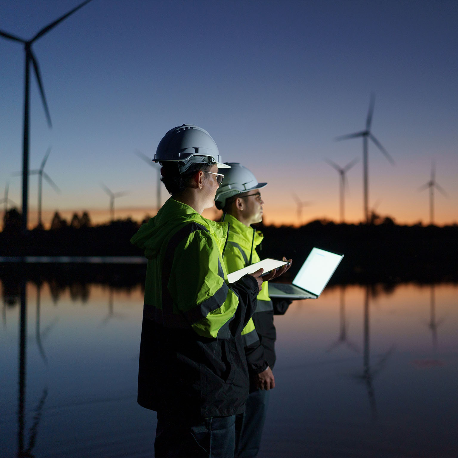 Engineers are checking the operation of a large wind turbine that is working to generate electricity in a wind farm during sunset.