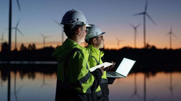 Engineers are checking the operation of a large wind turbine that is working to generate electricity in a wind farm during sunset.