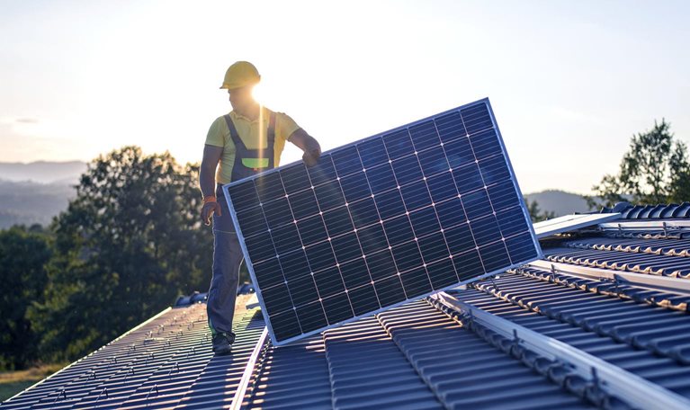An image of a worker installing solar panels on the roof of a house.