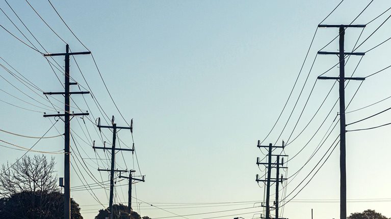 Electric poles with many cables located along rural country road with clear blue sky in background