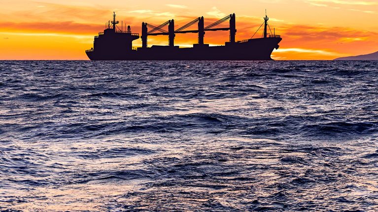 Cargo ship with grain at sea at sunset.