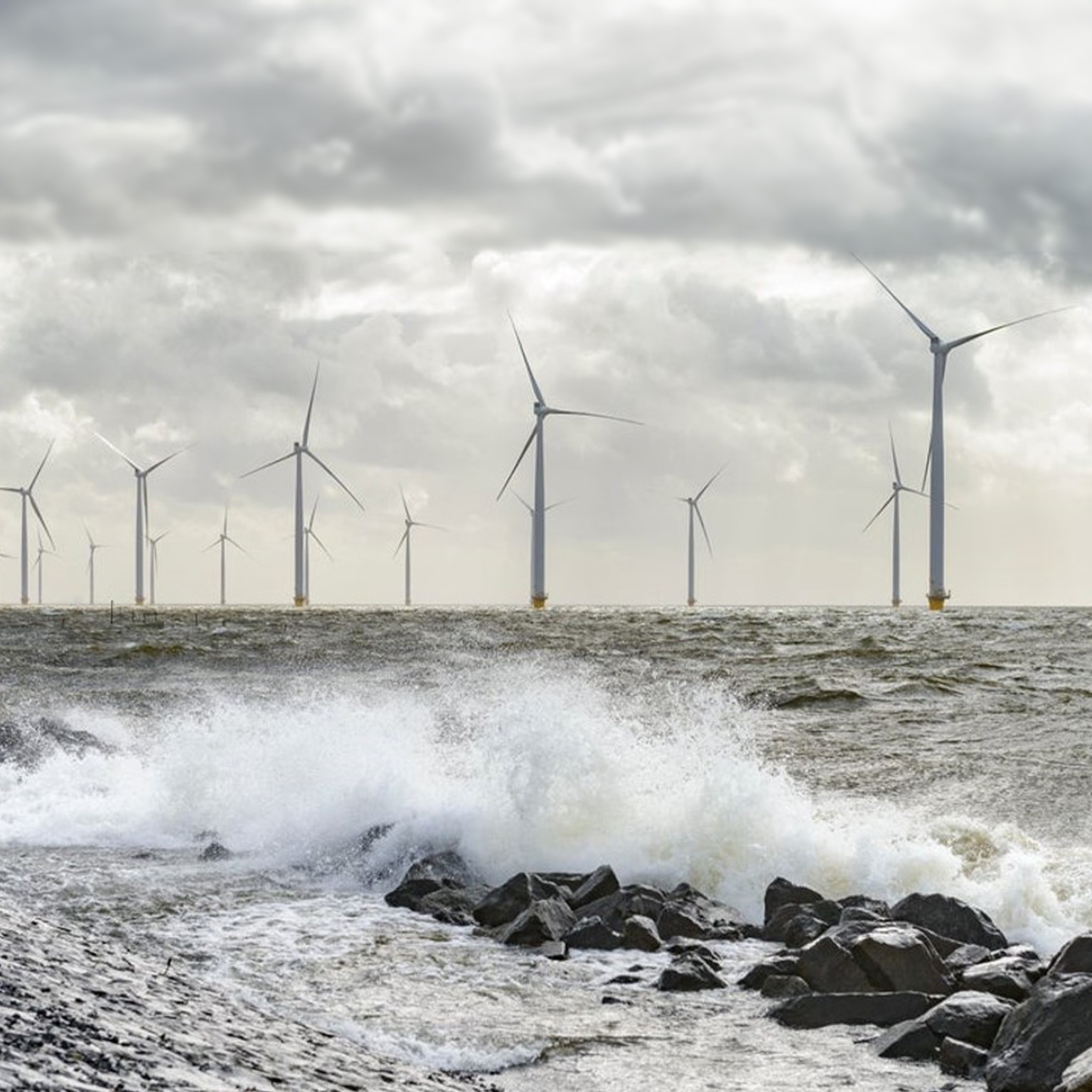 Offshore wind turbines during a storm as waves crash against rocks