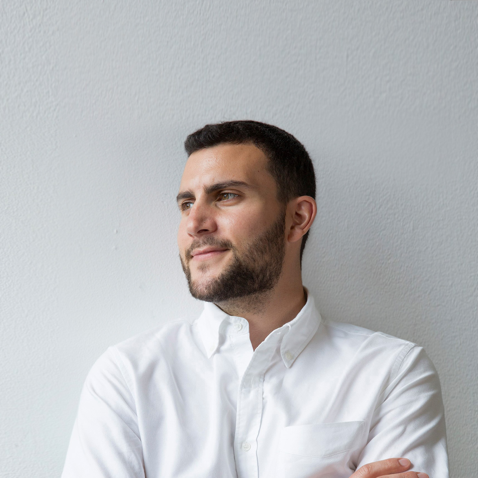Portrait of Forage’s CEO Ofek Lavian. Lavian has a subtle smile and his face turned away from the camera as he looks off into the distance. He's wearing a white button down shirt and is leaning against a white textured wall.