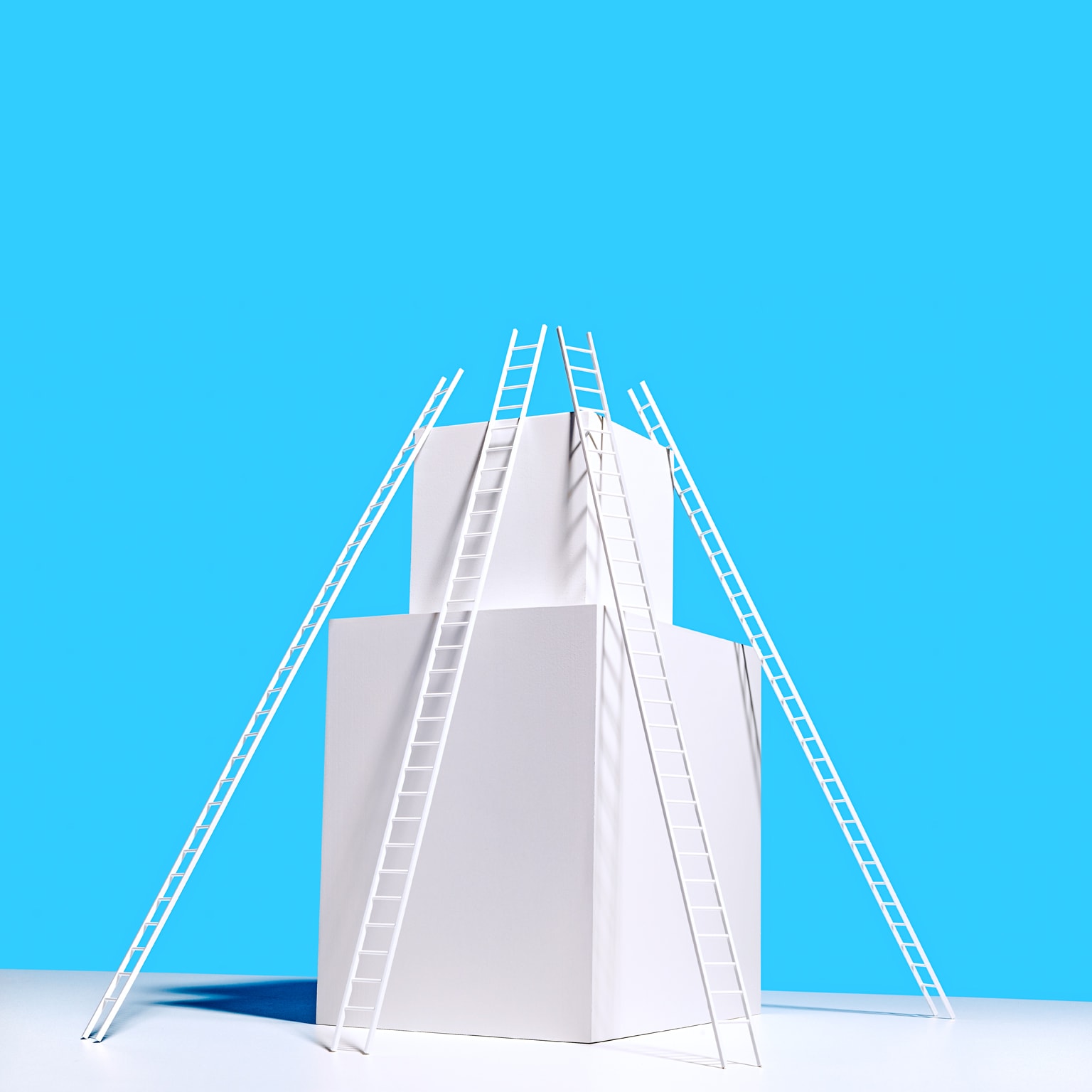 4 long white ladders resting on 2 stacked white boxes on white surface, blue background
