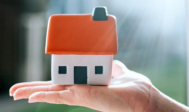 Model of a house with a red roof, held on a palm