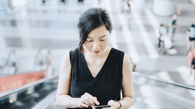 Young businesswoman reading emails on smartphone while riding on escalator