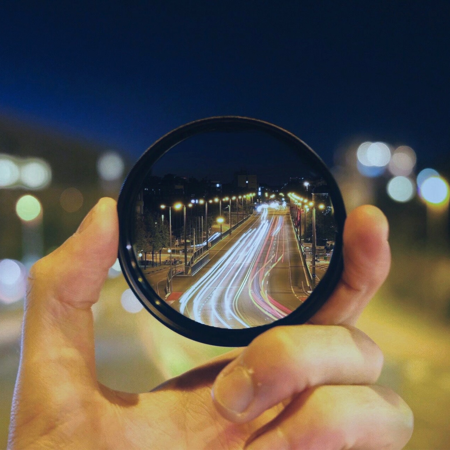 Close-Up Of Hand Holding Lens Against Road At Night