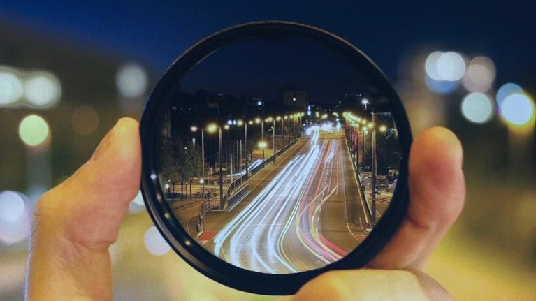 Close-Up Of Hand Holding Lens Against Road At Night
