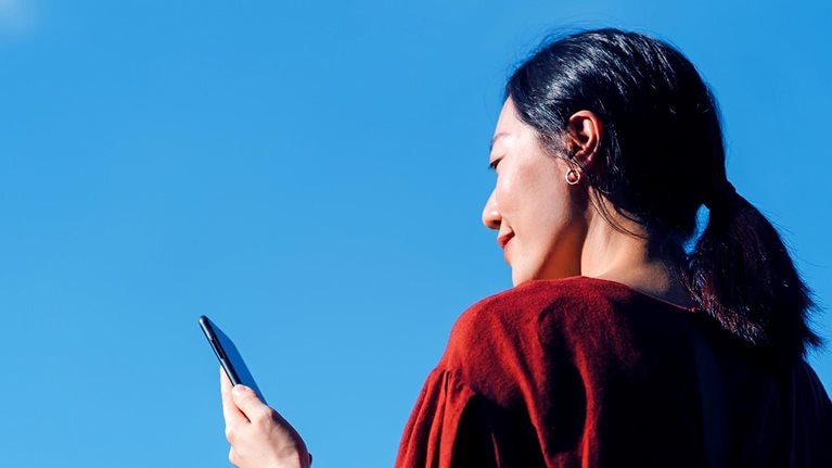 Low angle portrait of young Asian woman using smartphone against beautiful blue sky