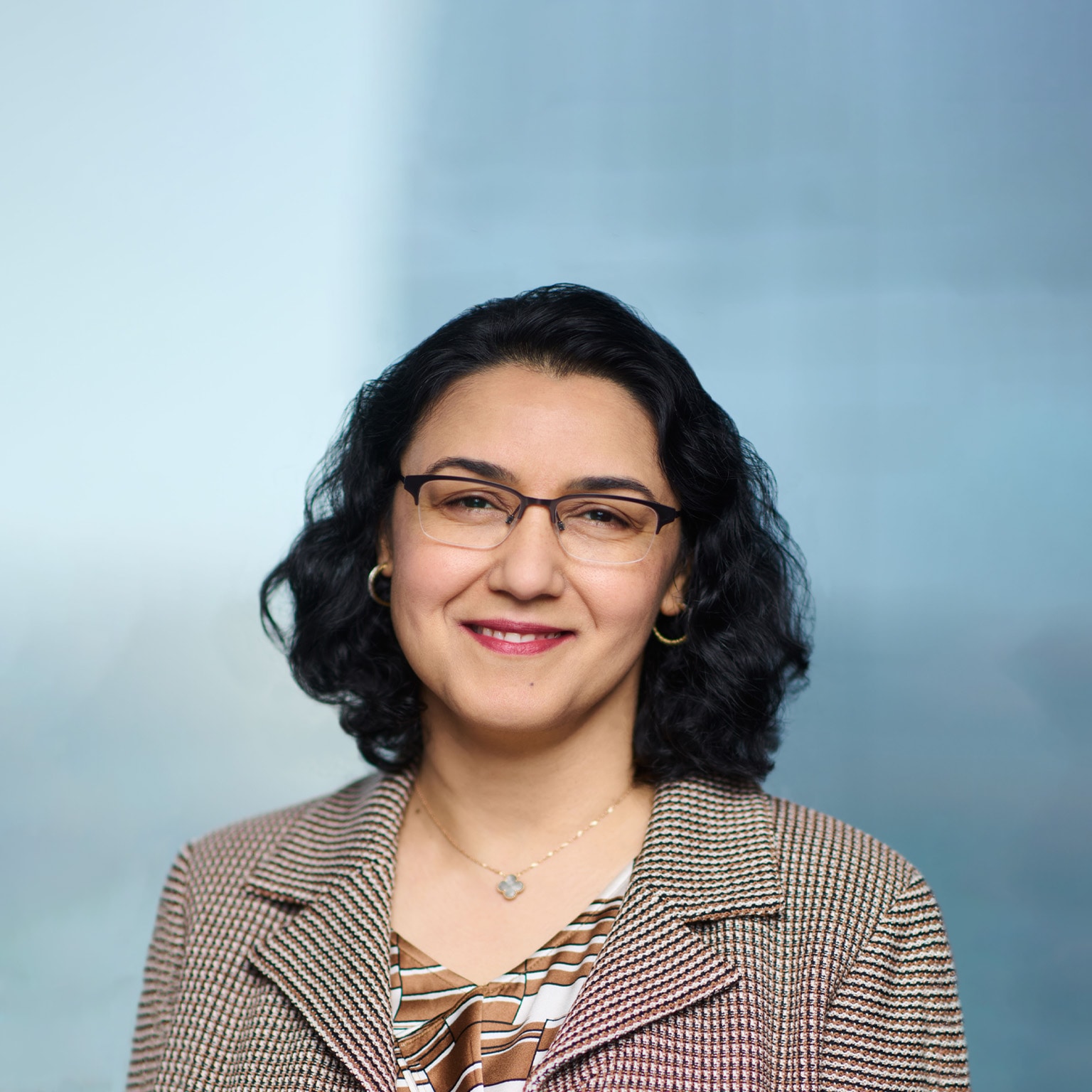 Portrait of a smiling Neeti Bhalla Johnson against a soft blue backdrop. 
