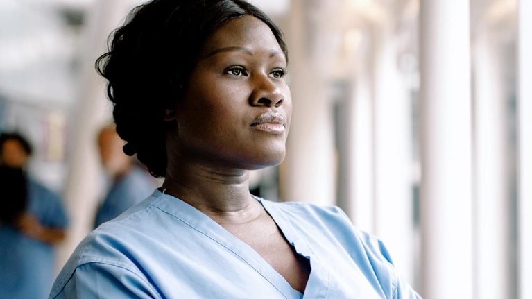 Contemplating female nurse with arms crossed looking through window in hospital