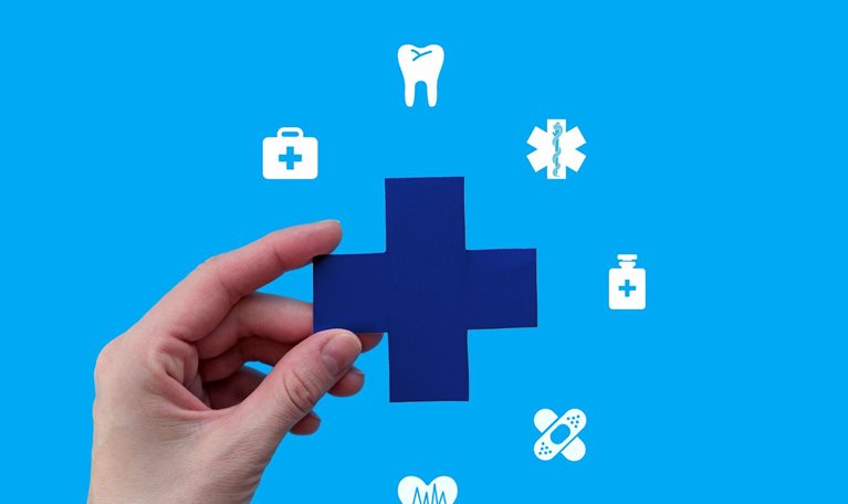 A hand holds a blue medical cross against a bright blue background. Surrounding the cross are various white medical icons, symbolizing comprehensive healthcare services.