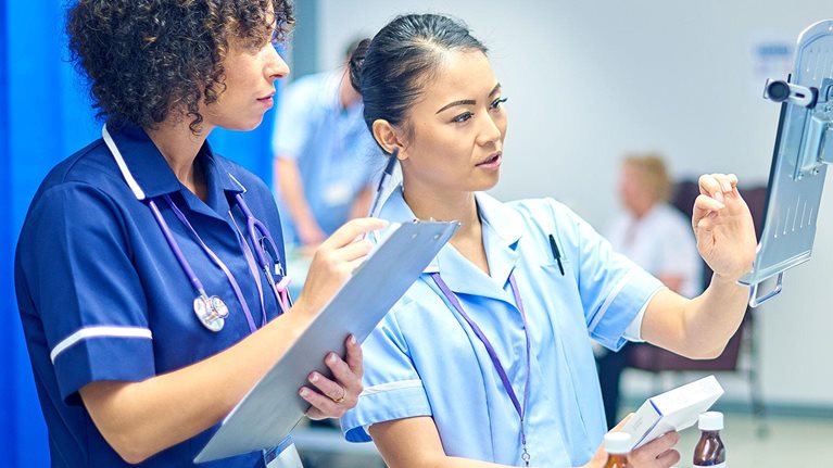 A young nurse checks the dosage on her digital tablet supervised by her staff nurse