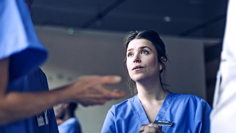 An attentive nurse, whose face shows a look of thoughtful consideration and slight apprehension, having a discussion with another nurse in a hospital hallway.
