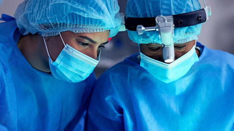 Surgeon, doctor and team in operating room for surgery, face mask or PPE for safety and healthcare at hospital. Help, support and medical procedure with medicine, trust with partner and treatment