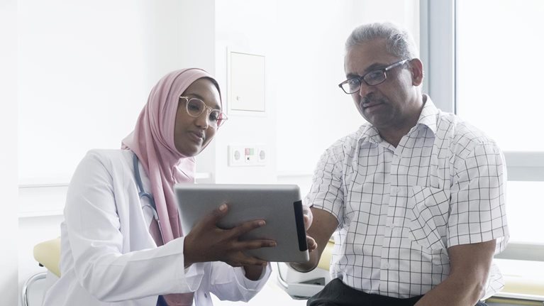 Female muslim doctor talking to senior patient using digital tablet