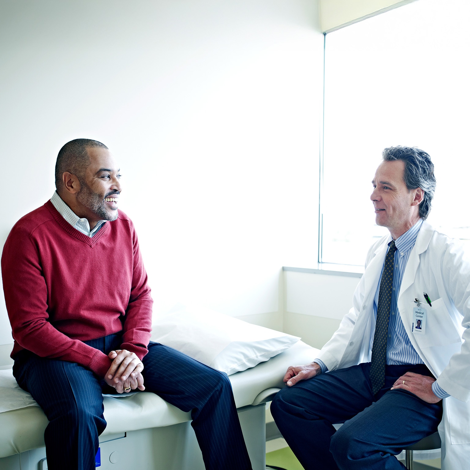 Mature male patient sitting on exam table in discussion with their doctor