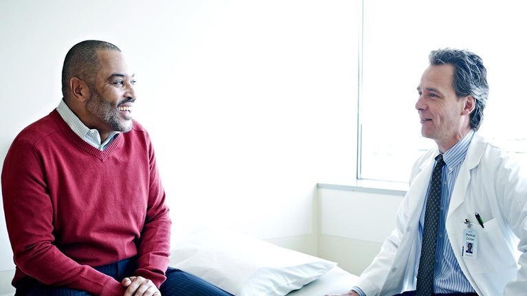 Mature male patient sitting on exam table in discussion with their doctor