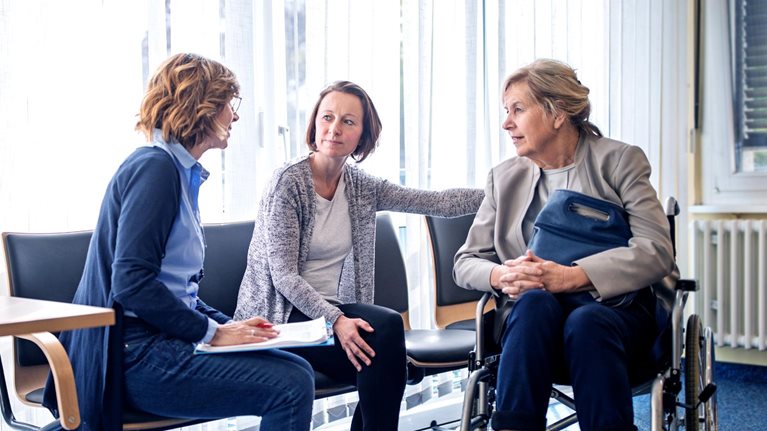 A social worker talking to an elderly woman in a wheelchair and her daughter in a hospital setting.