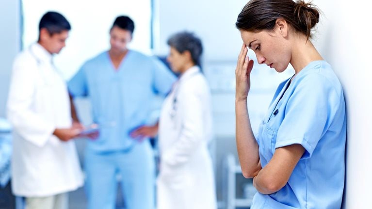 It's been a long shift. Shot of an exhausted doctor leaning against a wall with colleagues in the background. - stock photo